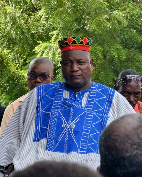 Un chef coutumier en boubou brodé et bonnet rouge, entouré de sa famille.