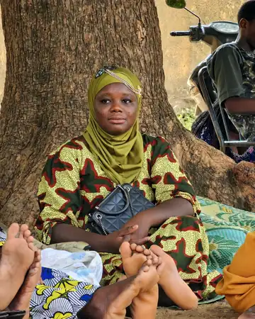 Une femme en voile vert assise au pied d'un arbre.