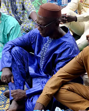 Un aîné en boubou bleu et bonnet brun.